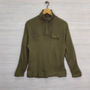 May include: Olive green long-sleeve pullover shirt with a mock neck and a quarter-zip closure. The shirt features a small pocket on the chest and is hanging on a wooden hanger.