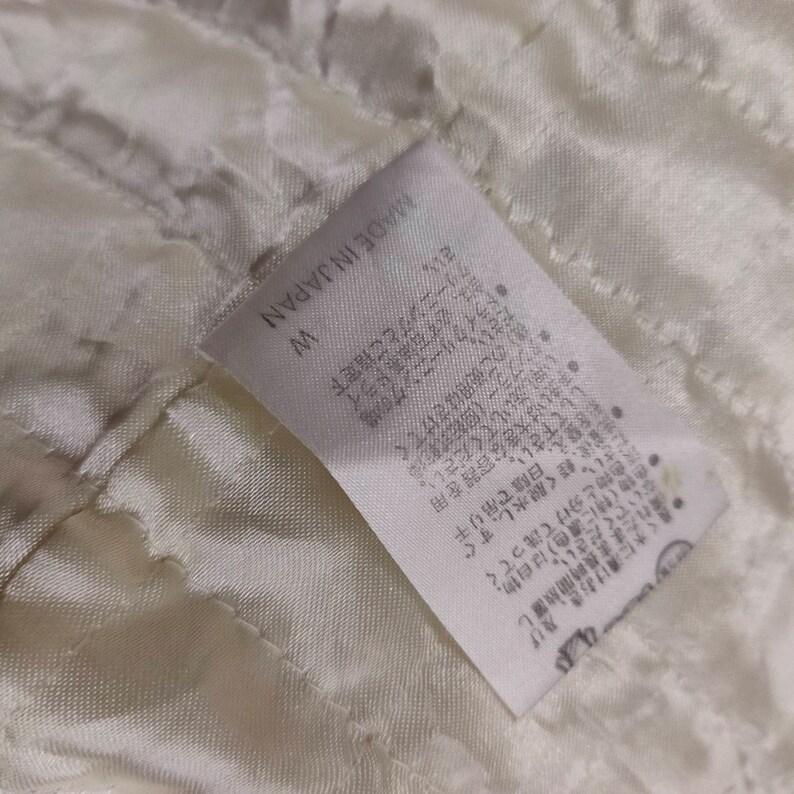 May include: White fabric tag with black text that reads "W MADE IN JAPAN". The tag has instructions for washing and dry cleaning the garment in Japanese.