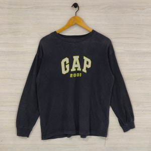 May include: A dark blue long-sleeved t-shirt with a white "GAP" logo and "2000" printed in yellow below it.