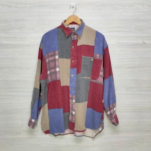 Puede incluir: Una camisa de manga larga con patchwork en una variedad de colores, incluyendo rojo, azul, gris y beige. La camisa tiene una botonadura frontal, un bolsillo en el pecho y un cuello. La tela parece suave, posiblemente franela.