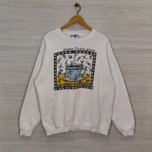 Può includere: Felpa bianca con una grafica di rane che saltano in una tazza di caffè. La grafica è circondata da una cornice gialla con un bordo nero. Il testo "Jumpin' Java Beans" è stampato sopra la grafica.