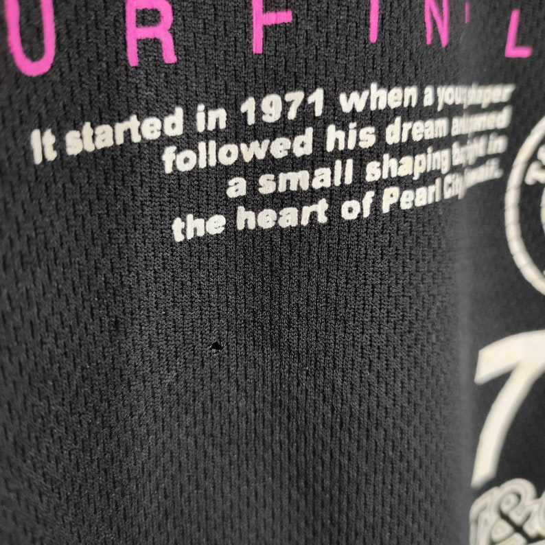 May include: Black t-shirt with white text that reads "It started in 1971 when a young man followed his dream and built a small shaping business in the heart of Pearl City."