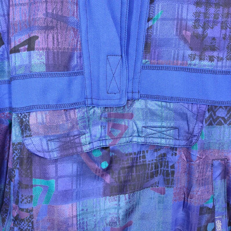 Puede incluir: Una tela con estampado azul y morado con una solapa azul y una X cosida en la solapa. La tela tiene un patr&oacute;n geom&eacute;trico.