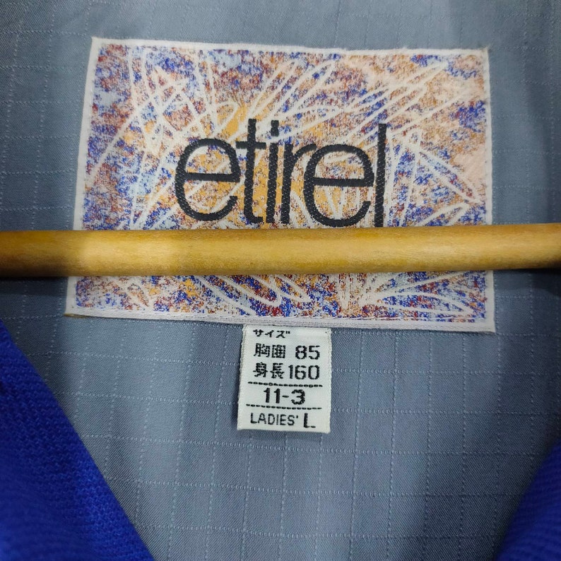 Puede incluir: Una chaqueta gris con cuello azul y una etiqueta que dice "etire" y "Talla: Cintura 85, Largo 160, 11-3, Damas L".