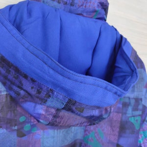 Puede incluir: Primer plano del interior de una chaqueta azul con capucha con un patr&oacute;n geom&eacute;trico en tonos azules, morados y verdes.