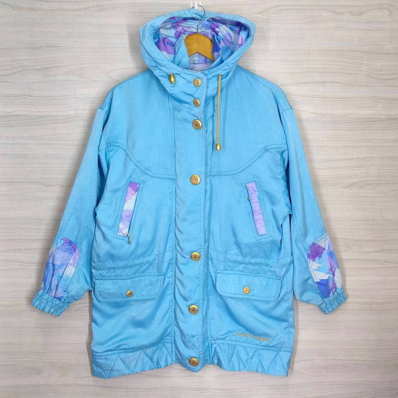 May include: A light blue hooded jacket with a floral print lining. The jacket has a gold zipper and buttons. The brand name "Sport-Vogue" is printed on the bottom left side of the jacket.
