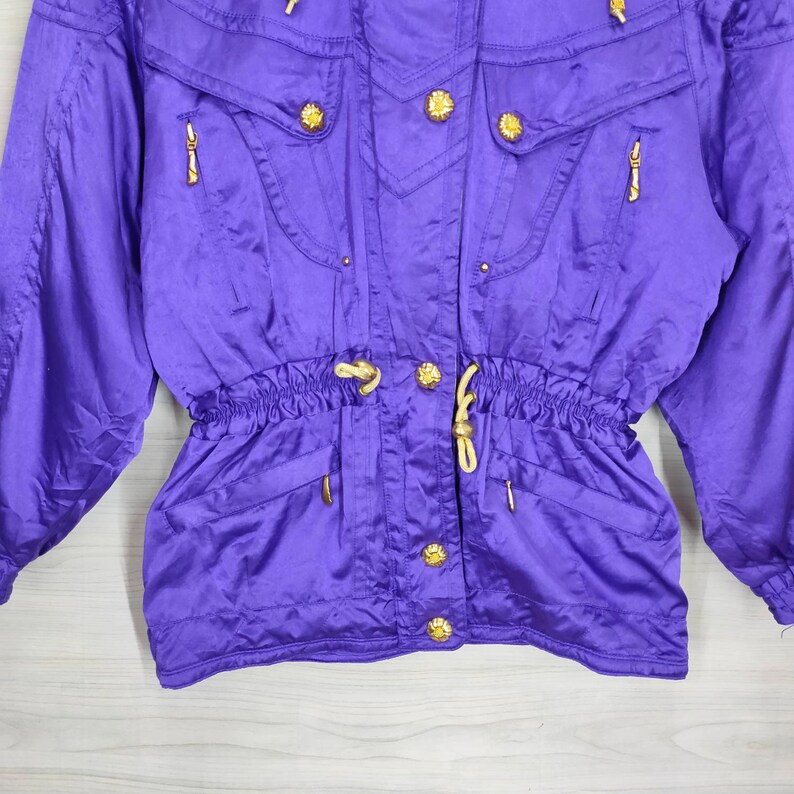 May include: Purple ski jacket with gold buttons and a drawstring waist.