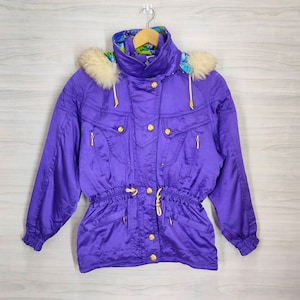 May include: A purple ski jacket with a white faux fur hood and gold buttons. The jacket has a drawstring waist and a floral lining.