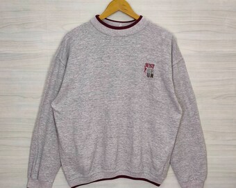 May include: A gray sweatshirt with a maroon ribbed collar and cuffs. The sweatshirt has the text "JUST FOR FUN" embroidered on the front in maroon.