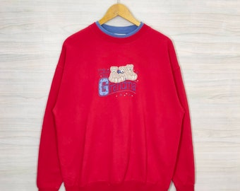 May include: Red sweatshirt with a blue inner collar and an embroidered design of three teddy bears with the word "Grandma" in blue lettering.