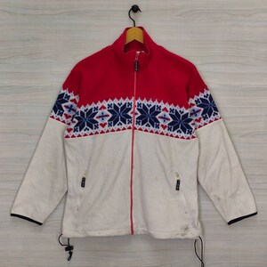 Peut inclure: Une veste en polaire blanche et rouge avec un motif de flocons de neige bleu et blanc. La veste a une fermeture éclair et deux poches.