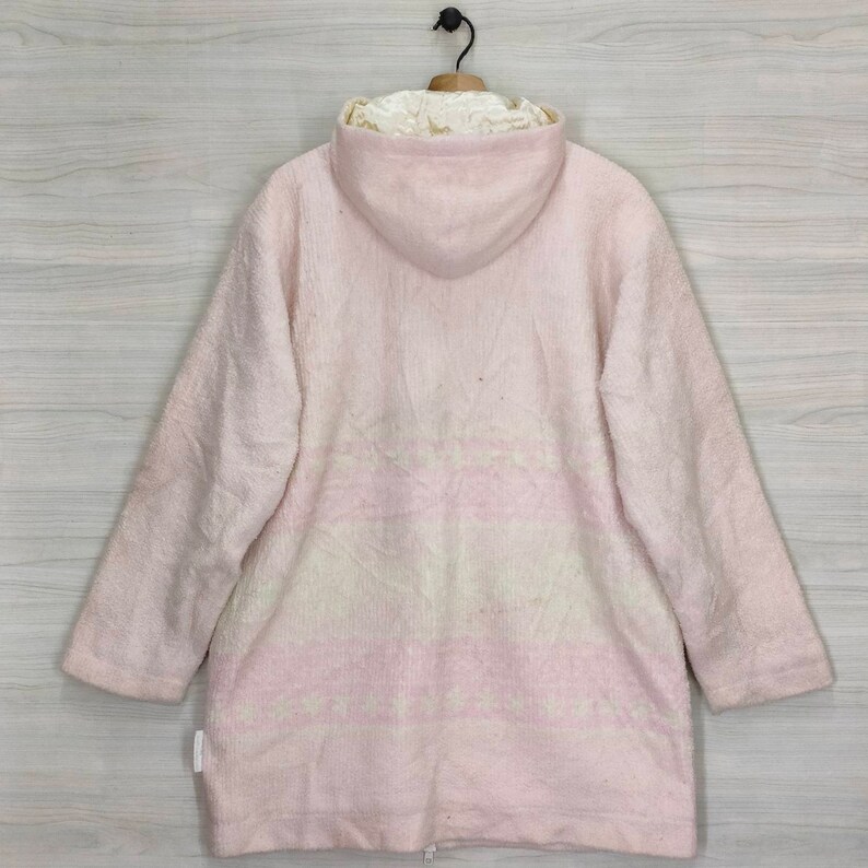 May include: A pink hooded jacket with a white and pink patterned design. The jacket is made of a soft, fuzzy material.