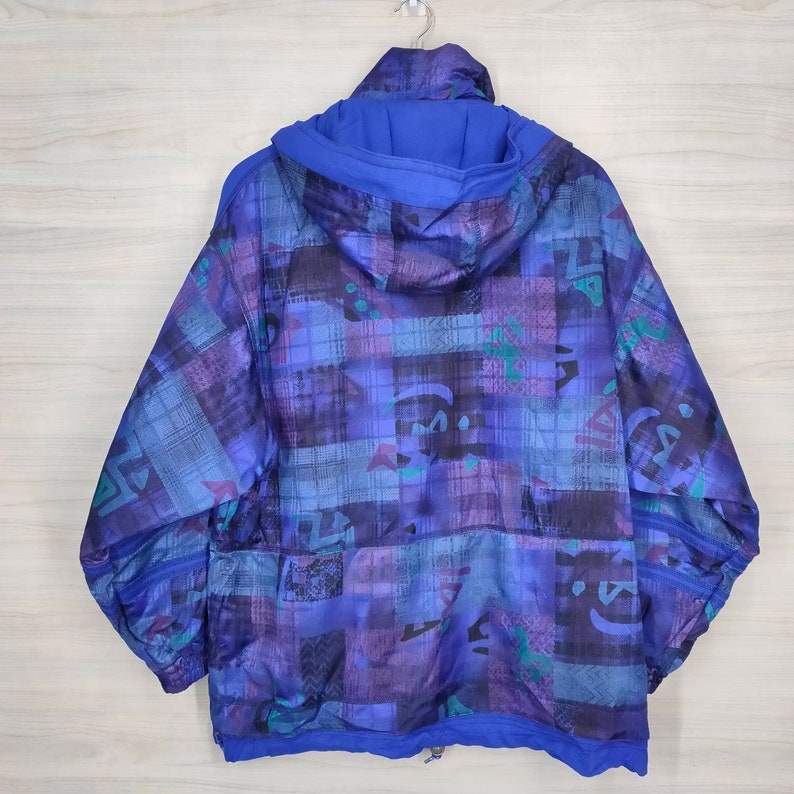 Puede incluir: Una chaqueta azul con capucha con un patr&oacute;n geom&eacute;trico en tonos de azul, morado y verde. La chaqueta tiene una cremallera y una capucha con cord&oacute;n.