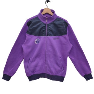 Puede incluir: Una chaqueta con cremallera de color morado con un panel negro en los hombros y el pecho. La chaqueta tiene un gran logotipo "P" en el lado izquierdo y el texto "Pro Line" en el lado derecho.