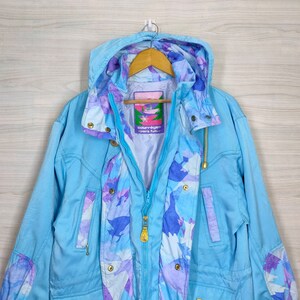 May include: A light blue jacket with a floral pattern lining. The jacket has a zipper closure, a hood, and two pockets. The label on the jacket reads "Courreges Sport Fuel".