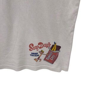May include: White t-shirt with a colorful graphic. The graphic features the text "Surf Day's UNDER THE SUN" in red and a cartoon character holding a chocolate bar. The chocolate bar is labeled "CHOCOLATE".