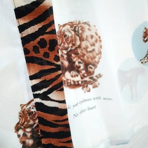 May include: White fabric with a brown and black tiger stripe pattern on the right side. The fabric has a print of a snow leopard on the left side. The text "'le your eyebrows with mine. No other heart" is printed on the fabric.