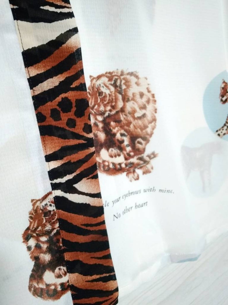 May include: White fabric with a brown and black tiger stripe pattern on the right side. The fabric has a print of a snow leopard on the left side. The text "'le your eyebrows with mine. No other heart" is printed on the fabric.