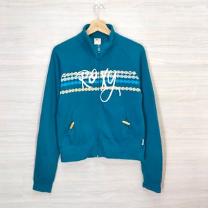 May include: Teal blue zip-up jacket with a white "Roxy" logo and a striped pattern of white, blue, and yellow circles.