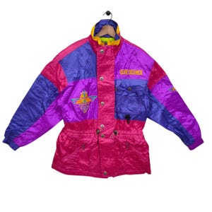 Könnte beinhalten: Eine Vintage-Skijacke in einem lebendigen Colorblock-Design. Die Jacke hat Einsätze in Pink, Lila und Blau mit gelben Akzenten am Kragen. Auf der Brust der Jacke steht das Wort "ESTERO" und ein Logo auf der linken Brust.
