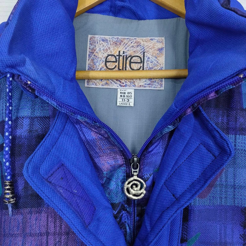 Puede incluir: Una chaqueta azul con estampado de cuadros y cierre de cremallera. La chaqueta tiene capucha y una etiqueta que dice "etirel" y "M-L 85 160 11-3 LADIES L".