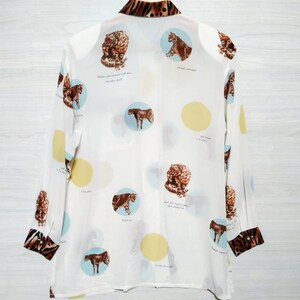 May include: White long-sleeved button-up shirt with a leopard print collar and cuffs. The shirt features a white background with a repeating pattern of circles containing leopard print images and text. The text reads: "Wings were given to us, not other burdens." "Fenced vineyard." "And beauty is in the eye." "What the world of pain has meant to me." "Though many waters cannot quench love." "It is a day in July." "Forget me not."