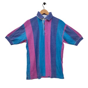 May include: A striped polo shirt with pink, blue, and purple vertical stripes. The shirt has a button-up collar and a single button closure at the neck.