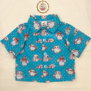 Op de afbeelding: Een blauw, kort mouwig overhemd met knopen, een wit stippenpatroon en een herhalend printje van een witte cartoonrobot met verschillende gezichtsuitdrukkingen. Het overhemd heeft een kraag en een knoopsluiting.