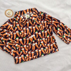 May include: A navy blue long-sleeved shirt with a festive pattern of carrots wearing Santa hats. The shirt has a button-up collar and long sleeves.