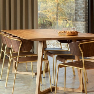 Op de afbeelding: Een houten eettafel met een lichte houtkleur en gouden metalen stoelen. De tafel is gedekt met een bord eten en twee glazen.
