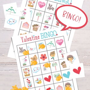 2 Valentines Day bingo cards are laid on top of each other  on a white table. There is a small pile of goldfish crackers. Six calling cards are scattered across the game, and several spots are marked with crackers. A word bubble says Bingo!