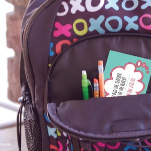 A zoomed-in image of a child's backpack with the pencil pocket open. The pocket contains pencils and a back-to-school lunchbox joke. Joke: Why did the teacher go to the beach? (Answer is not visible.)