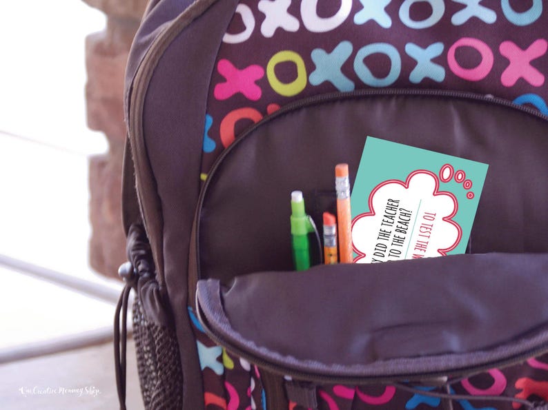 A zoomed-in image of a child's backpack with the pencil pocket open. The pocket contains pencils and a back-to-school lunchbox joke. Joke: Why did the teacher go to the beach? (Answer is not visible.)
