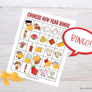 Chinese New Year bingo card lying on a white wooden table. Goldfish crackers are lying to the side of the board with several marking spaces on the bingo card. Five places are marked in a row, so there is a word bubble that reads, Bingo!
