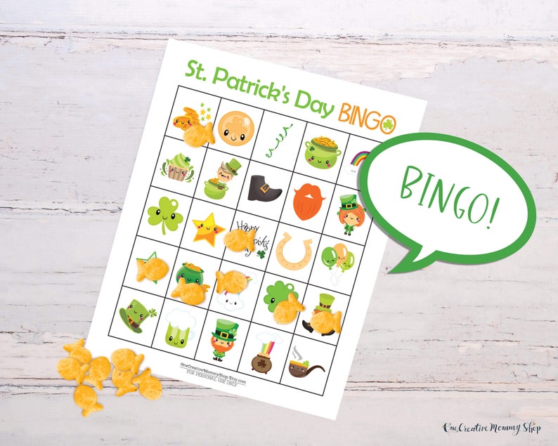 St. Patricks Day bingo card laying on a white wooden table. Goldfish crackers are laying to the side of the board with several marking spaces on the bingo card. Five places are marked in a row, so there is a word bubble that reads, Bingo!