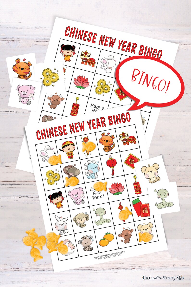 2 Chinese New Year bingo cards lying on a white table. Six calling cards are scattered across the game, and several spots are marked with goldfish crackers. A word bubble says Bingo!