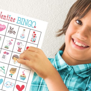 Cute smiling boy wearing a blue plaid shirt is proudly holding up a Valentine's Day bingo card