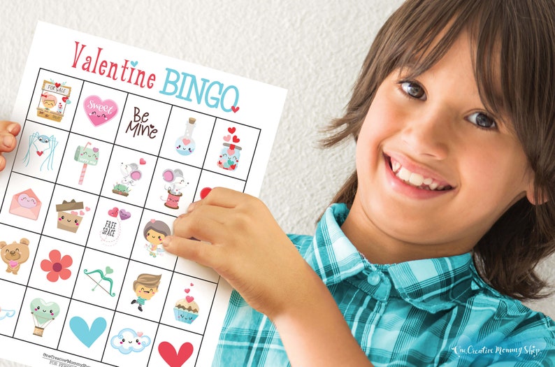 Cute smiling boy wearing a blue plaid shirt is proudly holding up a Valentine's Day bingo card