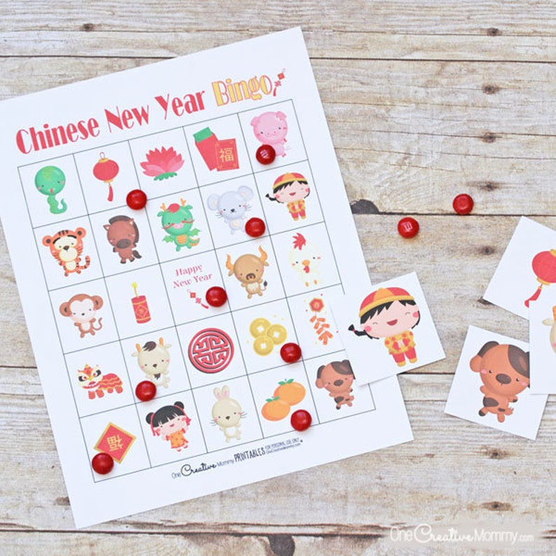 A Chinese New Year bingo game on top of a wooden table. The card is covered with chocolate candies, and three calling cards are showing. A Chinese boy, a dog, and a Chinese lantern.