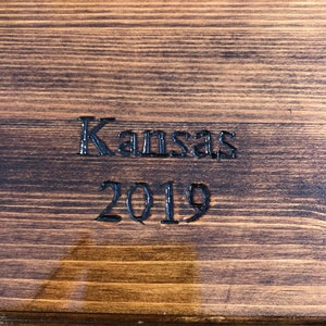 May include: A close-up of a wooden surface with the words "Kansas 2019" engraved in black.
