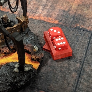 Può includere: Un porta dadi rosso con due dadi rossi, ognuno con punti bianchi. I dadi sono su una superficie strutturata, con un robot in miniatura e altri pezzi di gioco sullo sfondo. Scena di gioco da tavolo.