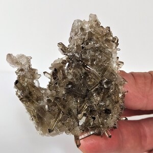 May include: A cluster of smoky quartz crystals with a variety of shapes and sizes. The crystals are a light brown color and have a translucent appearance.