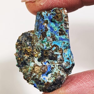 May include: A rough, irregular shaped piece of blue and green azurite and malachite mineral. The mineral has a dark brown, black, and gold matrix.