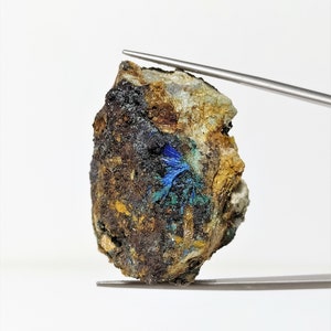 May include: A rough, brown, and gray rock with a small patch of blue and green crystals.