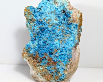 Puede incluir: Una roca rugosa de forma irregular con una formación mineral azul y marrón. El mineral azul parece ser una estructura cristalina, mientras que el mineral marrón es más terroso. La roca se muestra en un soporte de acrílico transparente.