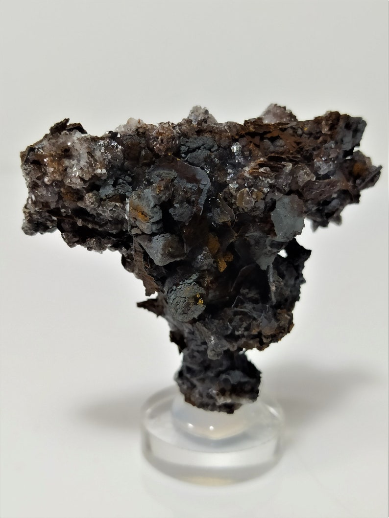 May include: A dark gray and brown mineral specimen with a rough, textured surface. The specimen is on a clear display stand.