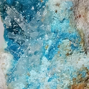 Op de afbeelding: Een close-up van een blauw en wit mineraalmonster. Het mineraal heeft een ruw, getextureerd oppervlak en is omgeven door een witte, rotsachtige matrix.