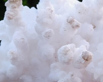 Op de afbeelding: Een grote, witte cluster van kristallen met een bloemkool-achtige textuur. De kristallen zijn doorschijnend en hebben een licht ruw oppervlak.