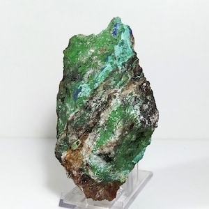 May include: A green and blue mineral specimen with a rough, textured surface. The specimen is mounted on a clear plastic stand.