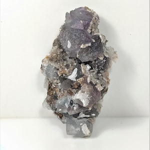 May include: A cluster of purple and gray fluorite crystals with a rough, natural texture. The crystals are clustered together in a random formation, creating a unique and interesting display.